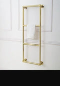 Gold-finished metal towel rail mounted on a white paneled wall, with a white towel draped over the middle bar.