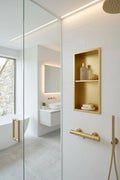 Modern bathroom interior with a gold-framed recessed shelf, gold towel bar, and gold shower fixture against white tiled walls and glass enclosure.