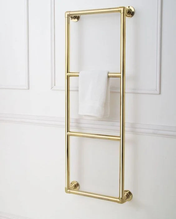 A vertical gold towel rail mounted on a white paneled wall, with a white towel draped over the middle bar.