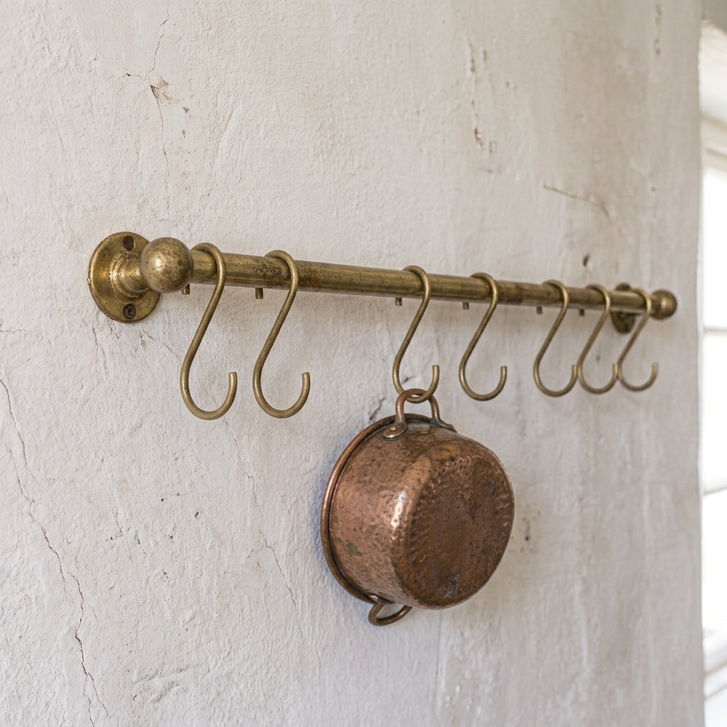 rod made of brass in aged brass finish used as a pot and pans rack installed on a white wall  with one pot