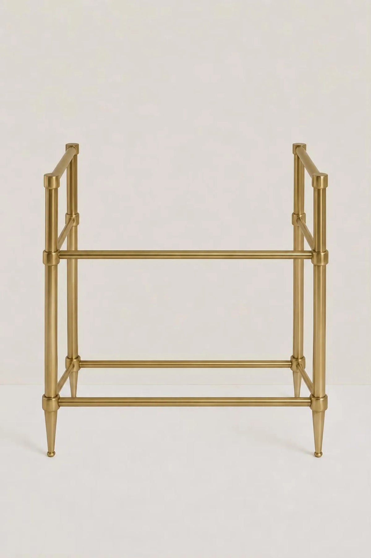 A gold-finished metal stand with a geometric frame design, featuring four legs with tapered ends and two horizontal bars, shown against a plain light background.