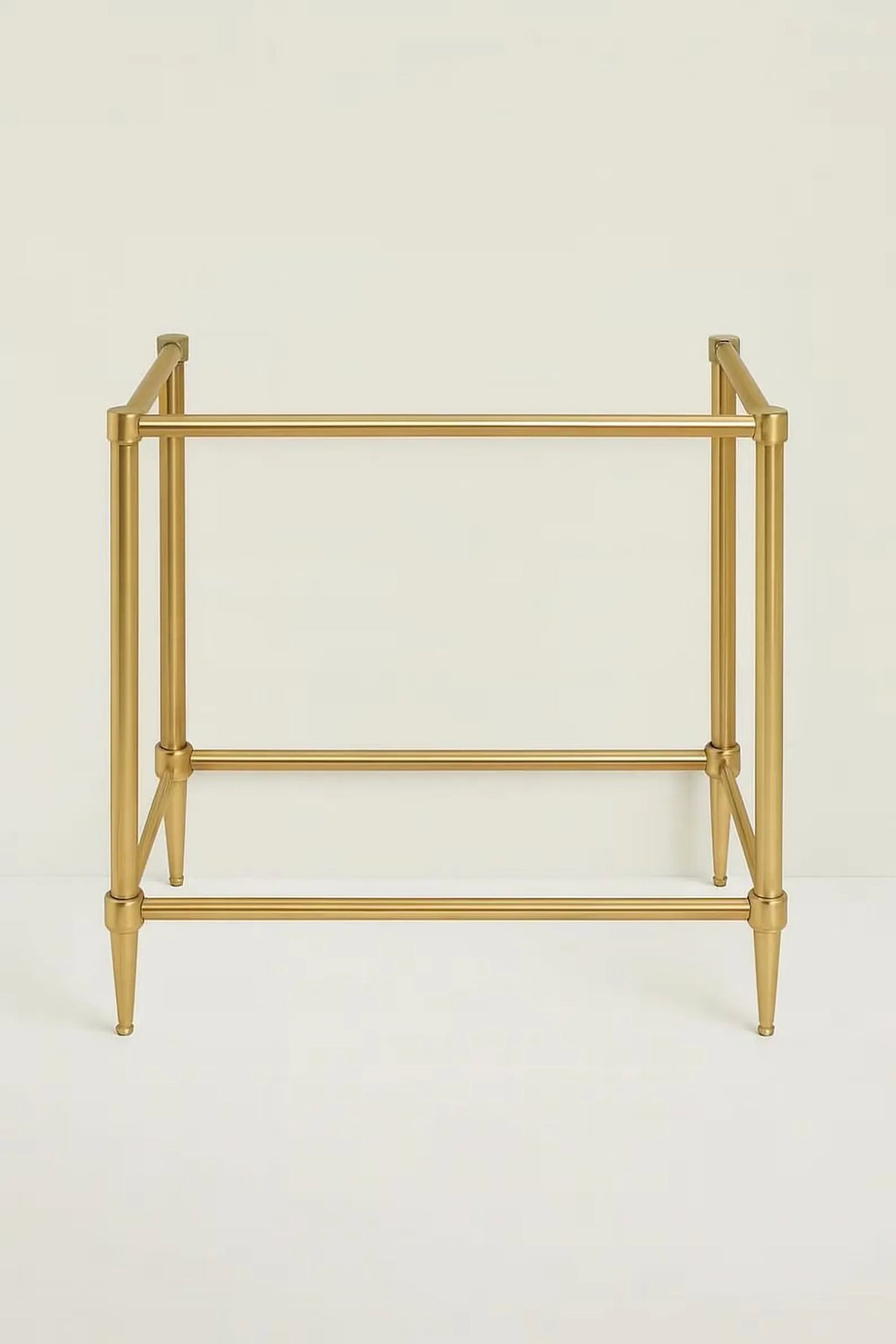 A minimalist gold metal side table featuring a geometric open-frame design with tapered legs and horizontal support bars, set against a plain off-white background.