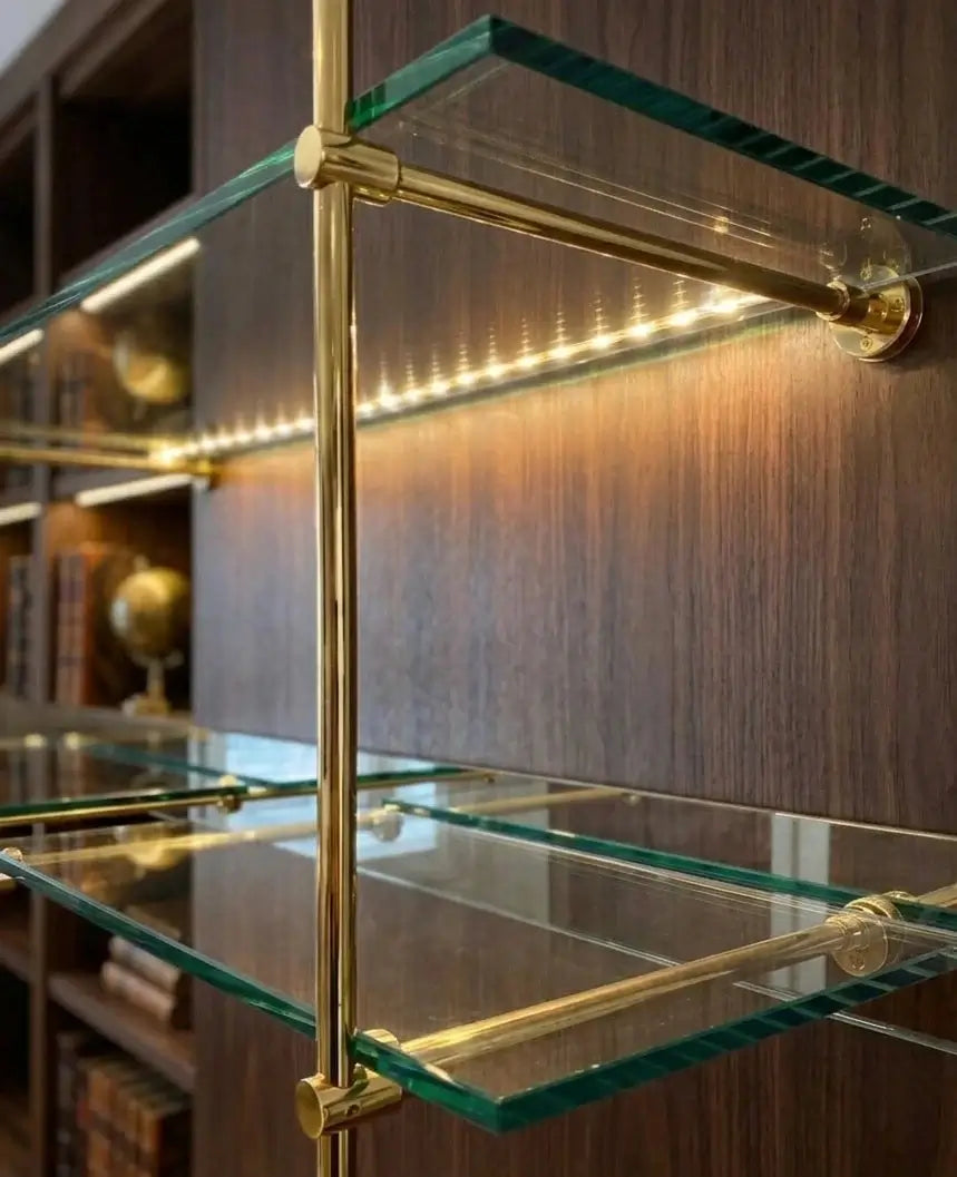 French Bistrot Shelves with brass brackets  in gold  ffinish and glass shelves against a wooden wall.