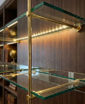 French Bistrot Shelves with brass brackets  in gold  ffinish and glass shelves against a wooden wall.