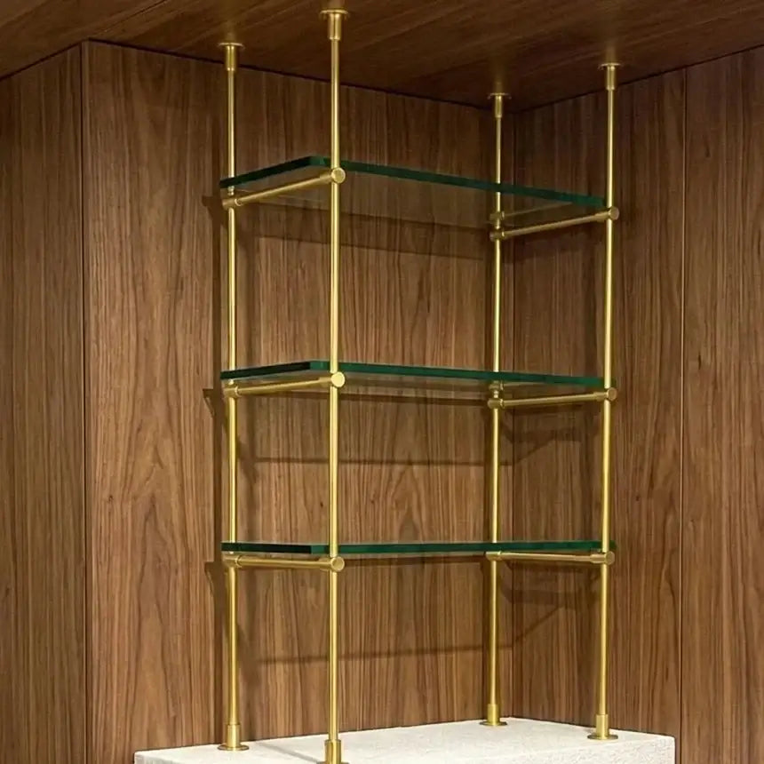 French Bistrot Shelves with brass brackets  in gold  ffinish and glass shelves against a wooden wall.