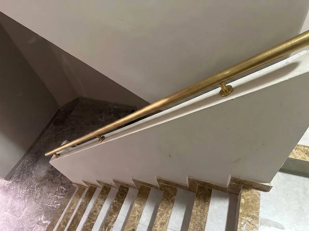A close-up view of a modern staircase featuring a brushed brass handrail mounted on white balustrade panels and beige stone steps.