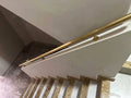 A close-up view of a modern staircase featuring a brushed brass handrail mounted on white balustrade panels and beige stone steps.