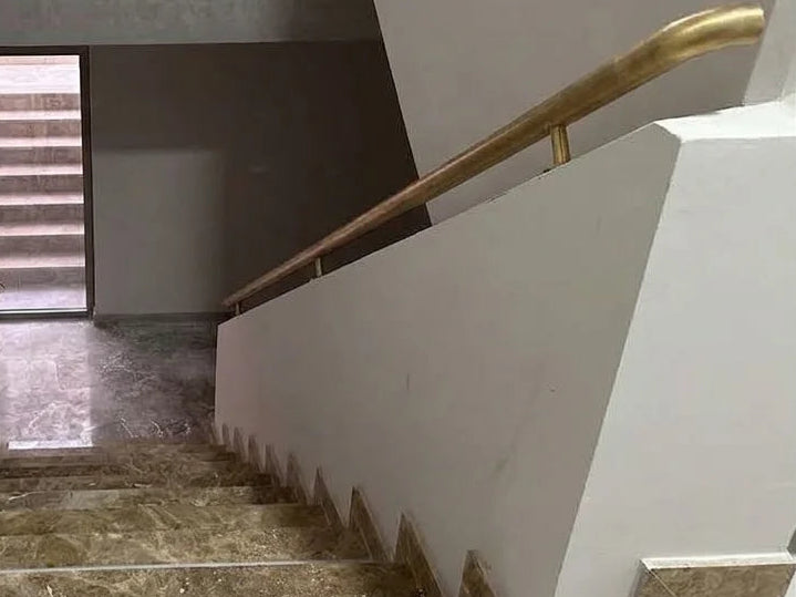 An interior staircase with marble steps, white walls, and curved brass handrails leading upward to a landing.