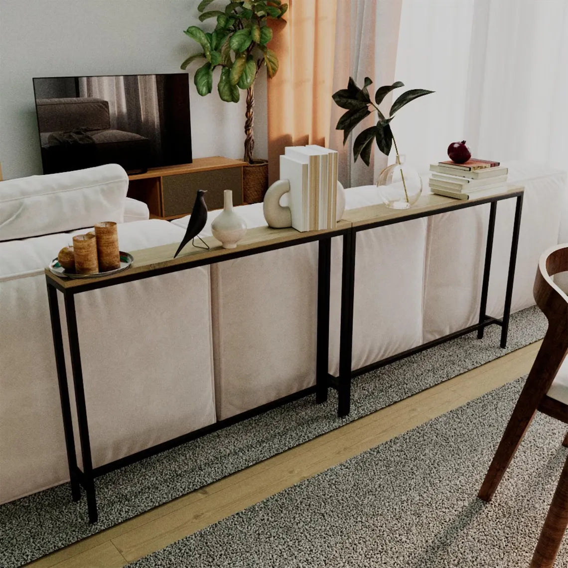 A long console table with a light wood top and black metal frame, styled in a modern living room setting next to a white sofa.