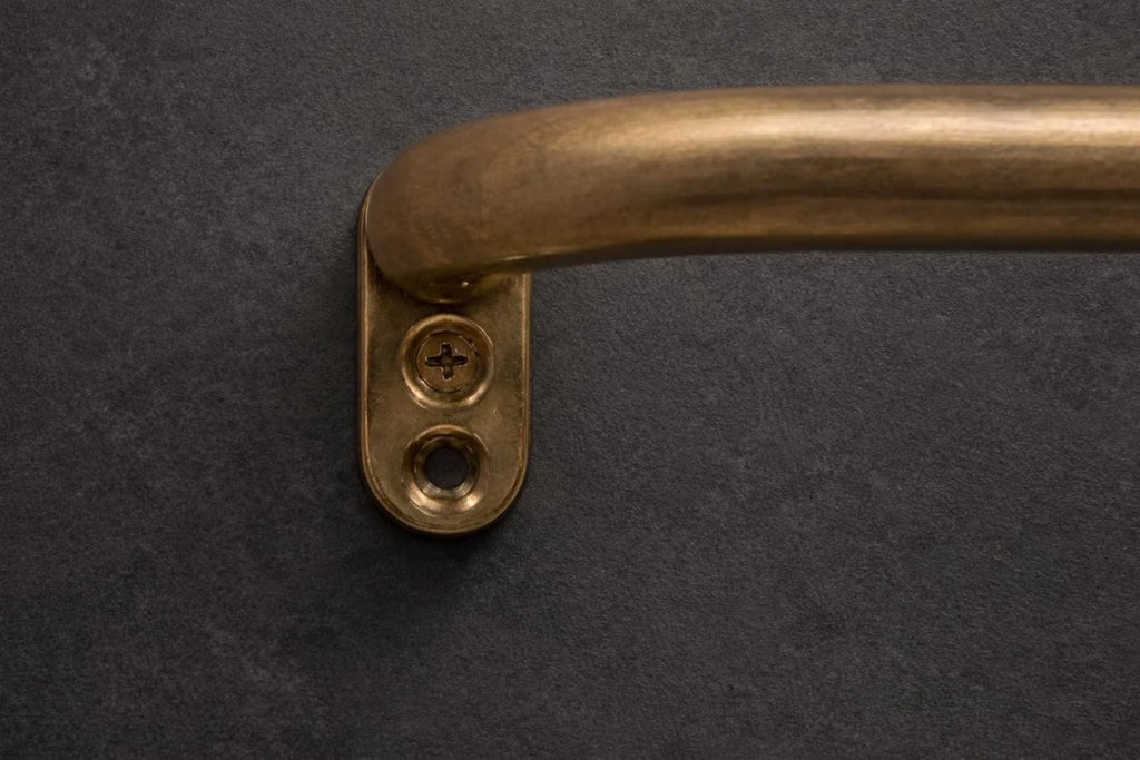 A close-up of a curved brass door handle mounted on a dark textured wall.