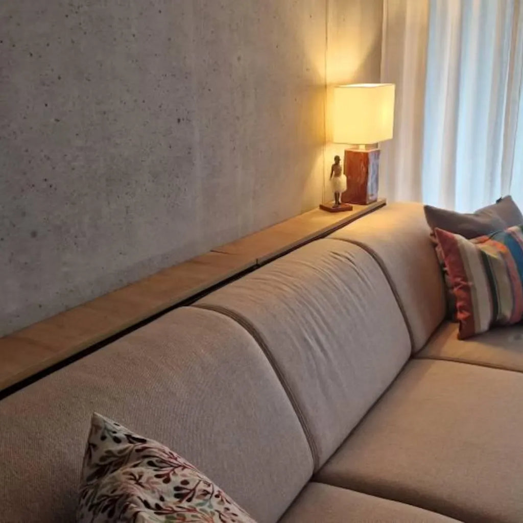 A modern beige sectional sofa in a contemporary living room setting, featuring a long wooden console table mounted along the wall, a lit table lamp, and patterned throw pillows.